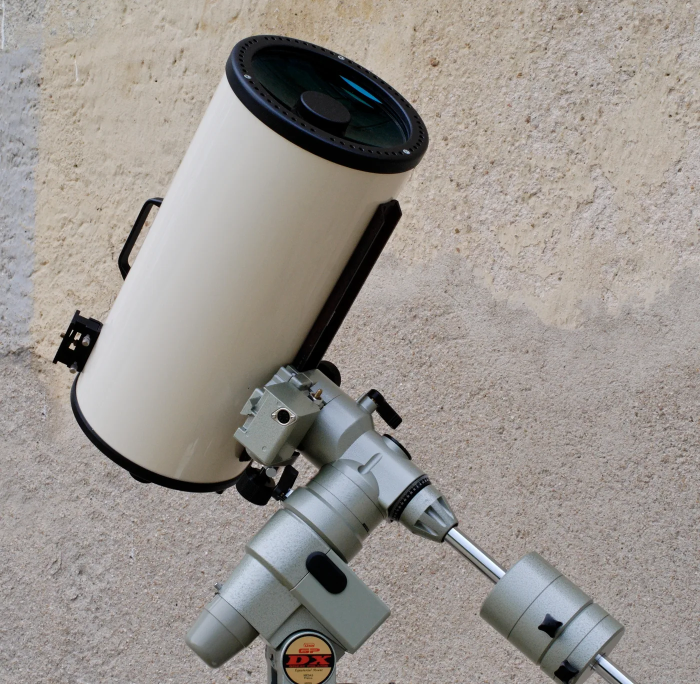 Tube blanc de Maksutov-Cassegrain incliné sur une monture équatoriale allemande, son ménisque frontal bleuté et le miroir secondaire circulaire collé en son centre bien visibles